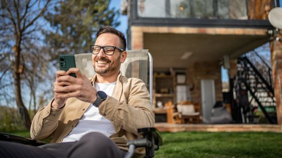 A cottager sitting on a chair using a smart electronic device.